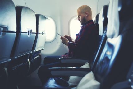 muškarac drži slušalice u avionu i sluša muziku